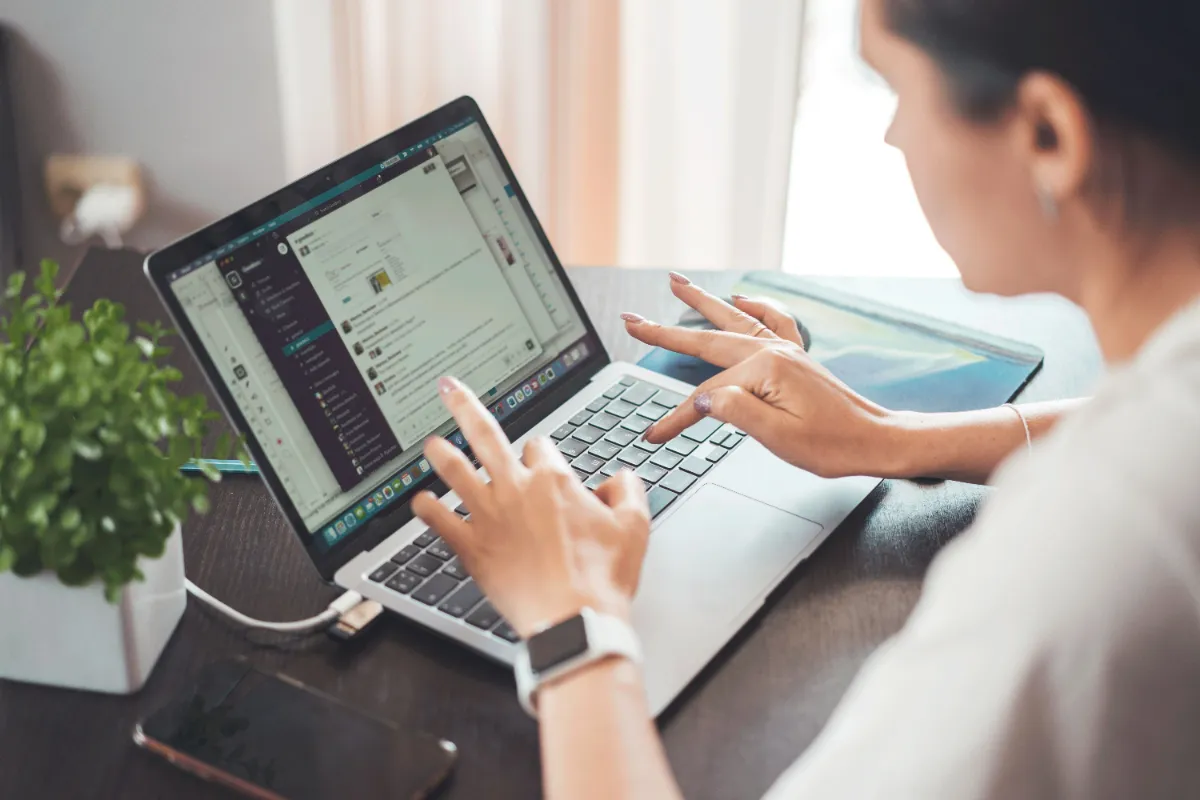 A person working at a laptop beside a tablet on a bright desk by a window